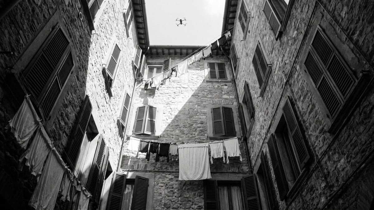 Cortile stretto di un palazzo italiano visto dal basso con un piccolo drone in volo tra le facciate, bianco e nero contrastato