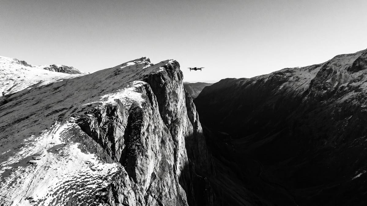 Cresta di montagna con strapiombo sulla valle e un piccolo drone in volo oltre il bordo, fotografia in bianco e nero